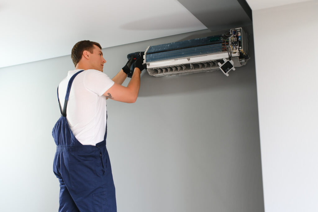 Man repairing a wall-mounted air conditioner unit during maintenance.